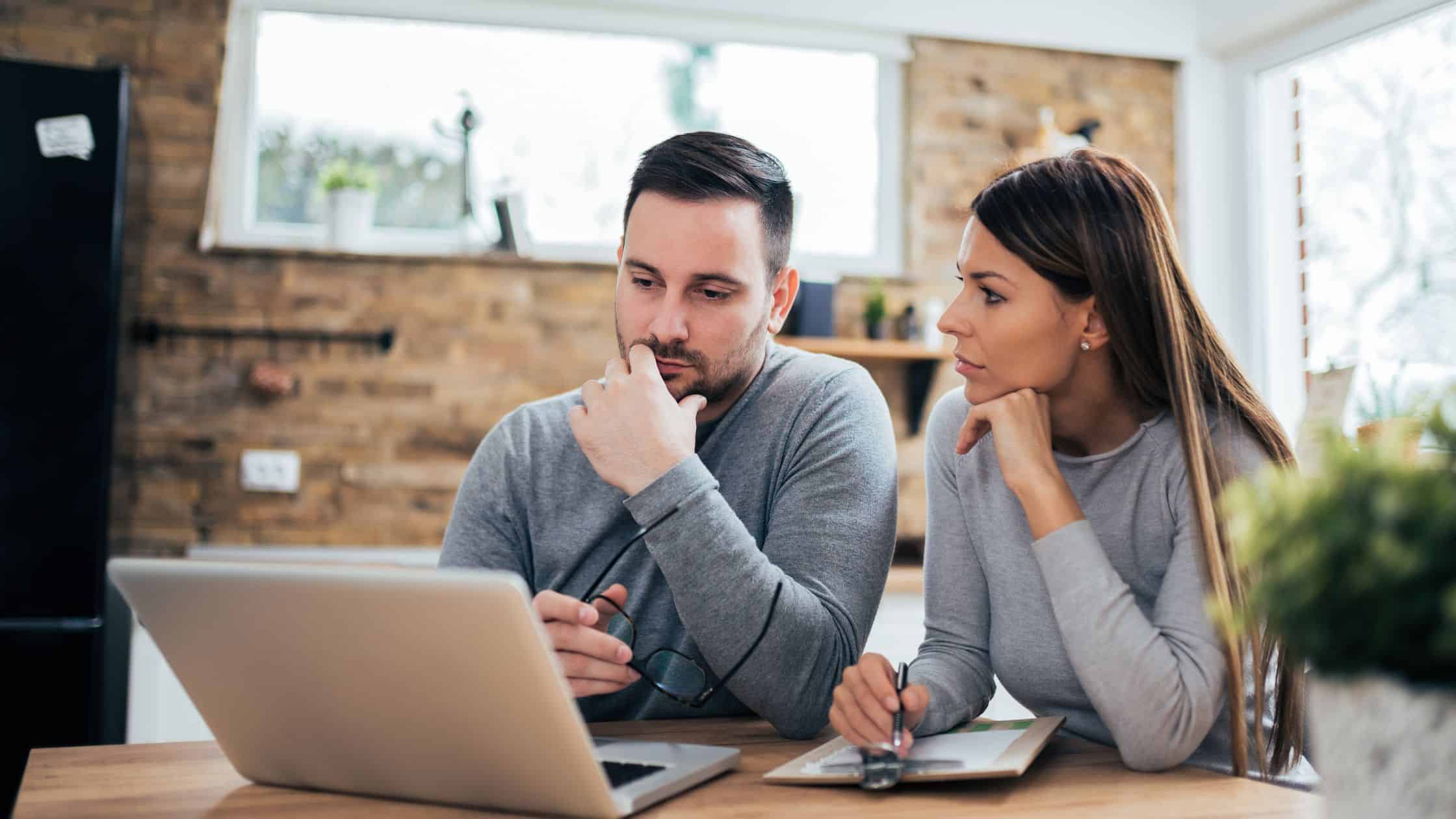 Couple reviewing financial documents during a divorce, highlighting the importance of agreeing a settlement early to avoid legal disputes.